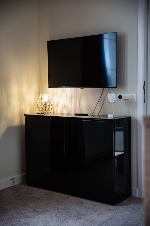 Chambre moderne de la Villa Bianca avec téléviseur mural au-dessus d'un meuble de divertissement noir, lampe décorative et prise murale blanche