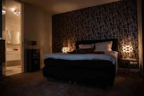 Chambre double moderne à la Villa Bianca avec mur d'accent à motifs géométriques, lampes de chevet éclairées et salle de bain attenante