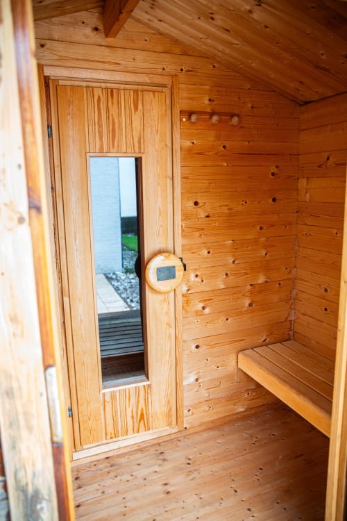 Intérieur du sauna en bois de la Villa Bianca B&B à Mortroux, Belgique, avec bancs et porte vitrée offrant une vue sur l'extérieur