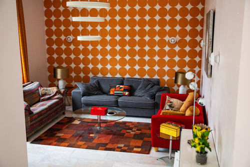 Salon moderne à la Villa Bianca avec papier peint à pois orange, canapé gris, fauteuil rouge et tapis à motifs à Mortroux