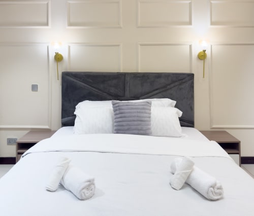 Modern bedroom in Cozy Apartments Ghana with charcoal headboard, white bedding, grey accent pillow, and brass wall sconces