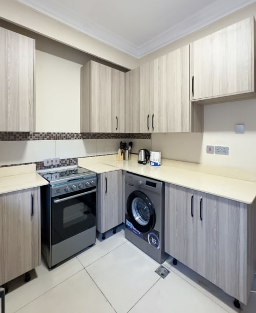 Modern kitchen in Capella Unit 4 at Cozy Apartments Ghana with stainless steel stove, washing machine, and light wood