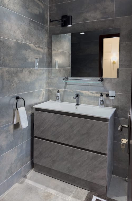 Modern bathroom in Capella Unit 4 at Cozy Apartments Ghana with gray tile walls, double vanity sink, and mirror at
