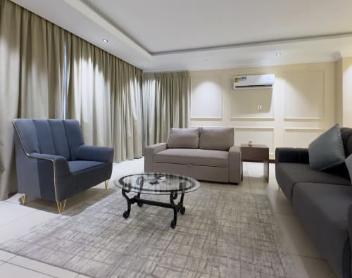 Modern living room at Cozy Apartments Ghana with blue armchair, gray sofa, and glass coffee table in Accra