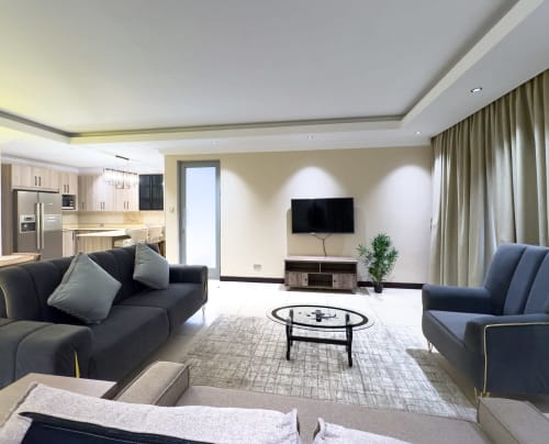 Modern living room in Capella Unit 4 at Cozy Apartments Ghana with black sofas, wall-mounted TV, and open kitchen view
