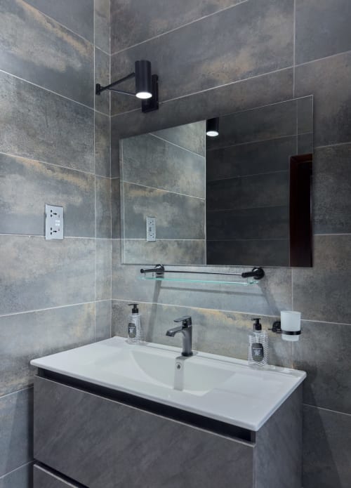 Modern bathroom vanity with dual sinks, gray tiled walls, mirror, and black fixtures in Cozy Apartments Ghana Capella Unit 4