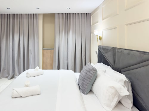 Modern bedroom in Capella Unit 4 at Cozy Apartments Ghana with gray upholstered bed, white linens, and floor-to-ceiling