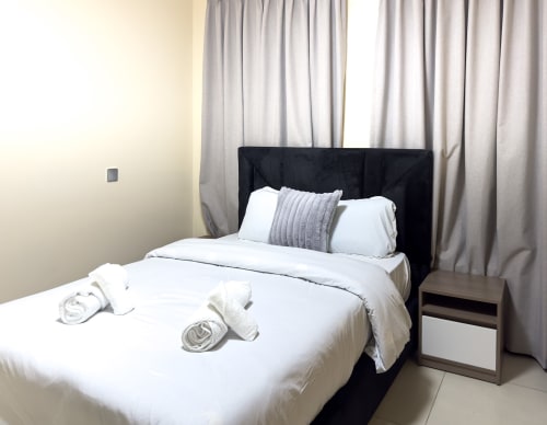 Modern bedroom in Capella Unit 4 at Cozy Apartments Ghana, Accra, with black bed frame, white linens, gray striped pillow,