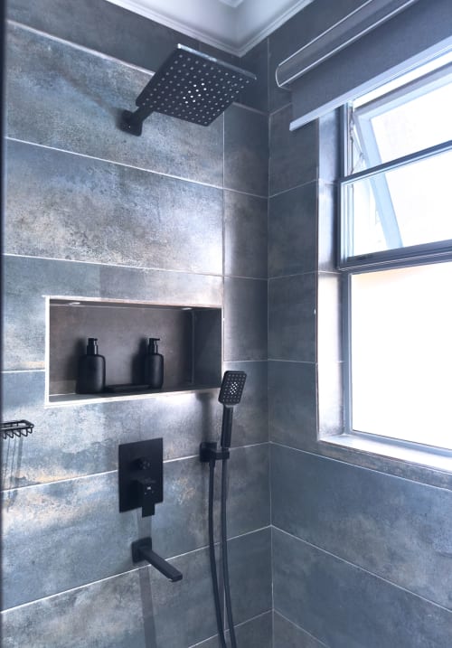 Modern shower with grey tile walls, rainfall showerhead, black fixtures, built-in niche with amenities, and window at Cozy