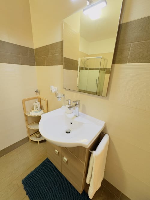 Modern bathroom at B&B Alba in Polignano a Mare with white sink, wooden vanity, mirror, and tiled walls