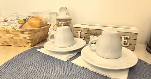 Breakfast setup in Camera Alba at B&B Alba, Polignano a Mare: white teacups with saucers, teapot, and bread basket