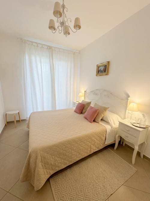 Camera elegante del B&B Alba a Polignano a Mare con letto in ferro bianco, biancheria color crema, cuscini rosa e vista sul giardino