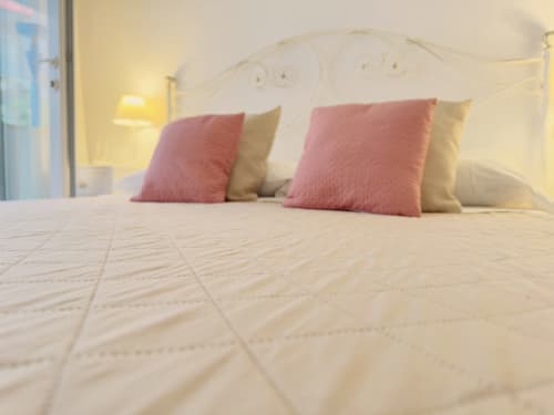 Cozy bedroom at B&B Alba in Polignano a Mare with cream quilted bedding, pink and beige pillows, ornate headboard, and warm