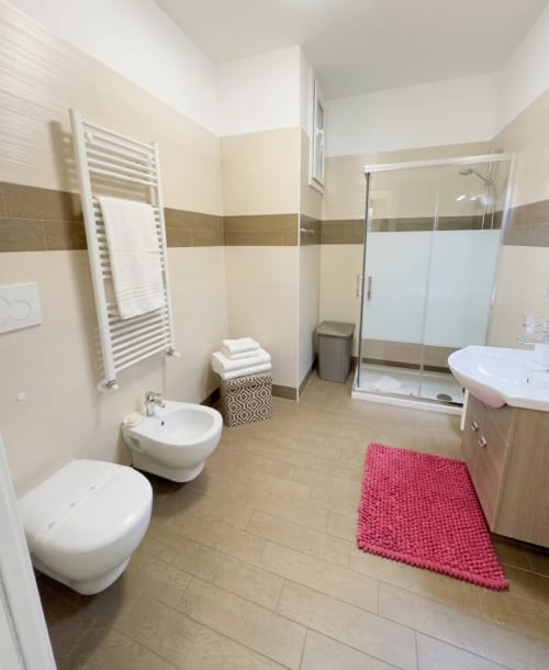 Modern bathroom at B&B Alba in Polignano a Mare with white fixtures, heated towel rail, glass shower enclosure, and pink bath