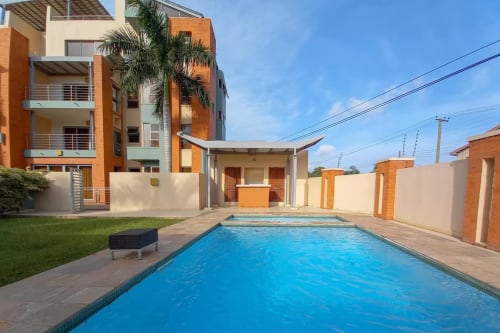 Cozy Apartments Ghana pool area in Accra with bright blue outdoor swimming pool, modern orange brick buildings, green lawn,