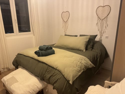 Chambre chaleureuse du Petit Coin de Paradis avec parure verte et crème, décoration murale en cœur et vue mer