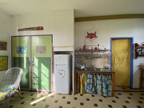 Colorful cottage kitchen with green cabinets, white fridge, and patterned blue textiles at Le Lama Zébré, Penmarch