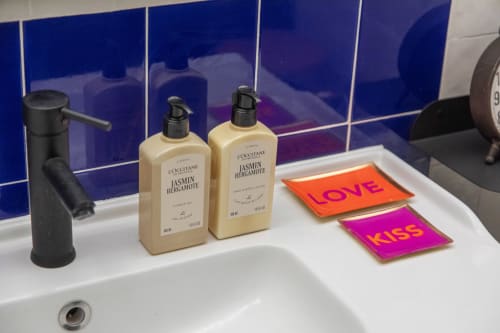 Produits de toilette L'OCCITANE Jasmin Bergamote et carreaux décoratifs 'LOVE' et 'KISS' sur le lavabo de la salle de bains de la maison d'hôtes Alombre
