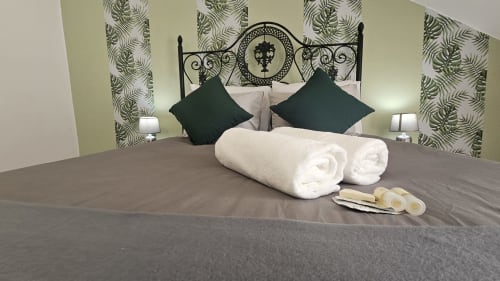 Quarto moderno de albergue em Lisboa com cama ornamentada preta, almofadas escuras, toalhas enroladas e papel de parede com padrão de samambaia