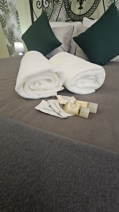 Toalhas brancas enroladas e amenidades de boas-vindas na cama com almofadas verdes no hostel Grupo Lisboa em Lisboa