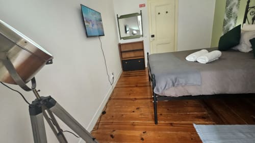 Quarto de hostel em Lisboa com piso de madeira, cama com toalhas brancas, TV, espelho, luminária de mesa e portas brancas