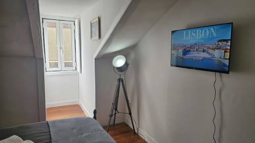 Quarto de hostel em Lisboa com TV, luminária de tripé, piso de madeira e vista da cidade na tela