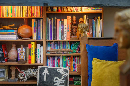 Eclectic wooden bookshelf at Alombre B&B Lectoure with colorful books, artifacts, and blue cushioned seating