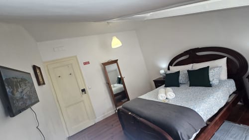 Quarto luminoso no hostel Grupo Lisboa Alojamentos em Lisboa com cama de madeira, almofadas verdes, toalhas brancas, TV de ecrã plano,