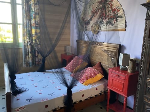 Chinesisch eingerichtetes Schlafzimmer im Le Lama Zébré in Penmarch mit Himmelbett, bunten Kissen und dekorativem Fächer