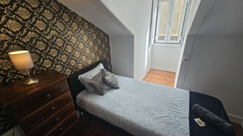 Quarto aconchegante no hostel Grupo Lisboa Alojamentos com papéis de parede ornamentados, criado-mudo de madeira e vista da cidade pela porta de vidro