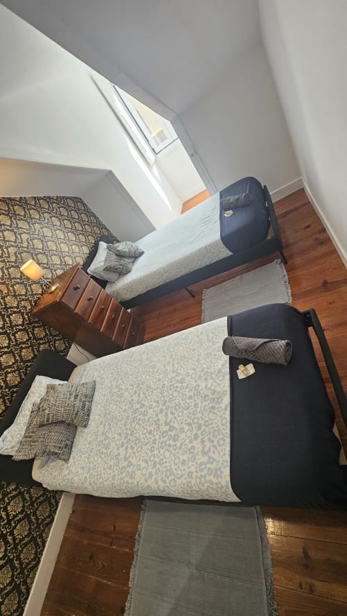 Quarto de hostel em Lisboa com duas camas, piso de madeira e vistas da cidade pela janela do teto inclinado
