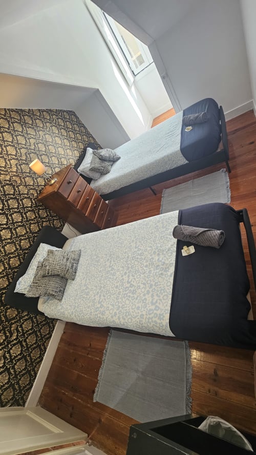 Dois camas de solteiro com roupa de cama estampada num quarto luminoso do Grupo Lisboa Alojamentos, piso em madeira e vista para a cidade
