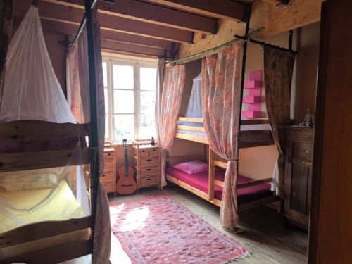 Shared girls' dormitory room with multiple wooden canopy beds, pink bedding, guitar, and window garden view at Le Lama Zébré