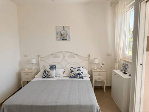 Camera luminosa al B&B Alba a Polignano a Mare con letto in ferro battuto, comodini color crema, vista giardino e arredamento costiero