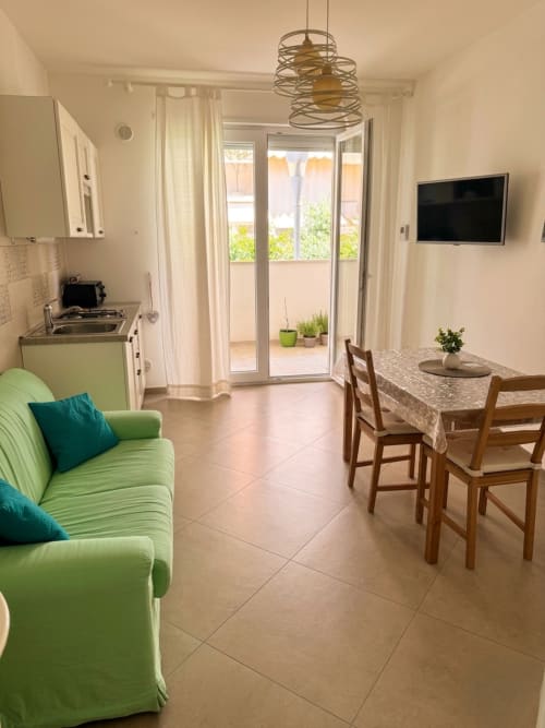 Camera luminosa e moderna al B&B Alba a Polignano a Mare con divano verde, tavolo da pranzo, angolo cottura e vista sul giardino