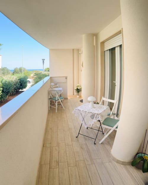 Balcone luminoso della B&B Alba a Polignano a Mare con vista sul giardino, pavimento in legno, sedie bianche e orizzonte marino visibile