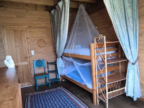 Shared bedroom at Le Lama Zébré in Penmarch with wooden bunk beds, mosquito netting, and blue curtains