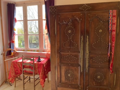 Rustic apartment bedroom at Le Lama Zébré in Penmarch with ornate wooden wardrobe, garden views, and traditional décor