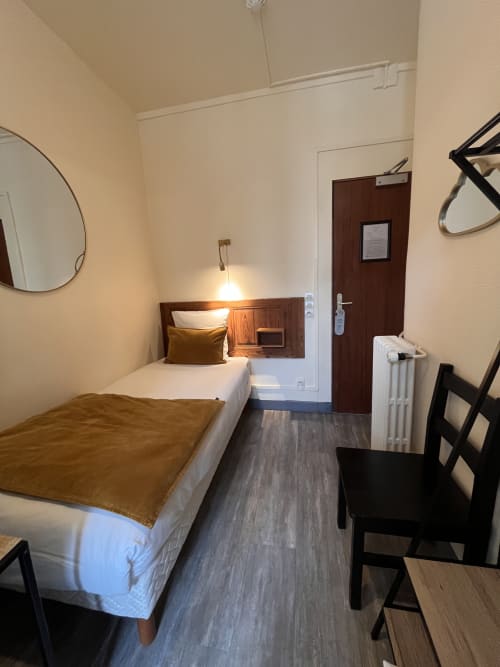 Compact single room at Hotel Le Trouville with single bed, wooden headboard, pendant light, mirror, and dark wood door