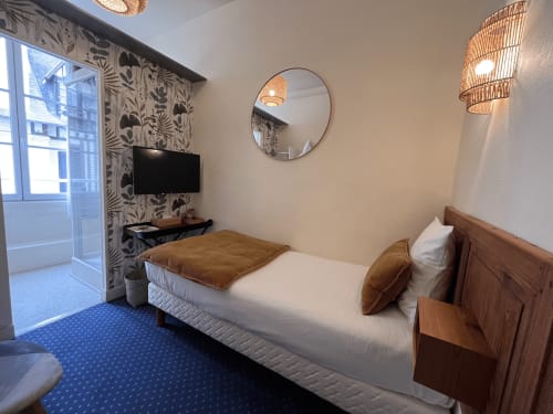 Modern single room at Hotel Le Trouville with wooden bed, flat-screen TV, round mirror, and city view from balcony door