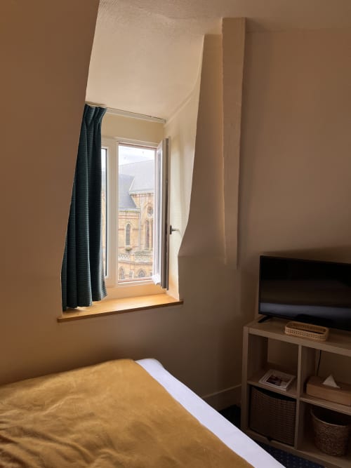 Bright hotel room with bed, TV, and window overlooking historic church in Trouville sur Mer