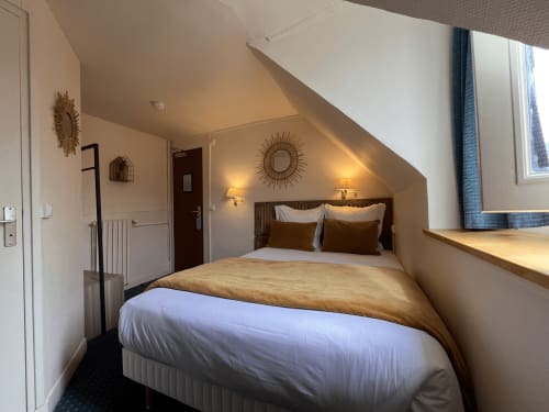 Cozy double bedroom at Hotel Le Trouville with queen bed, warm lighting, sloped ceiling, and seaside view in Trouville sur