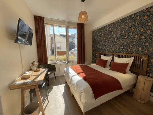 Modern hotel bedroom at Le Trouville with double bed, city view windows, patterned wallpaper, desk, and woven pendant light