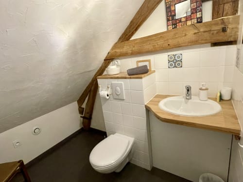 Salle de bain mansardée aux Prairies du Val d'Amboise : carrelage blanc, meuble vasque en bois, poutres apparentes