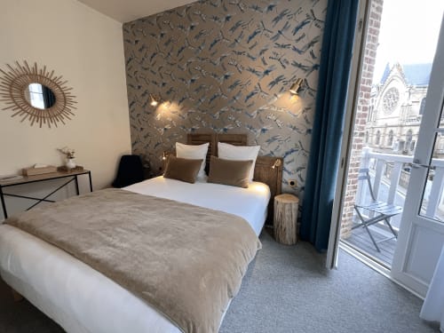 Modern hotel bedroom at Le Trouville with dual beds, bird-print wallpaper, and balcony overlooking Trouville-sur-Mer landmark