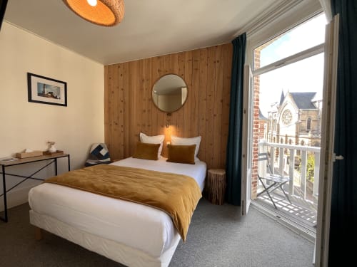 Bright bedroom at Hotel Le Trouville with wooden accent wall, balcony overlooking a church landmark, and modern amenities