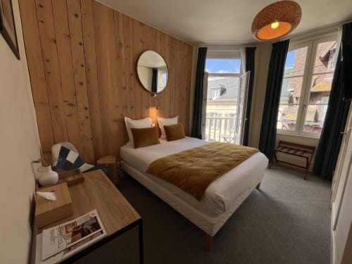 Modern bedroom at Hotel Le Trouville with wooden accent wall, balcony view of Trouville-sur-Mer, and coastal architecture