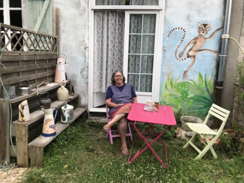 Woman relaxing in garden courtyard at Le Lama Zébré B&B, Penmarch, with outdoor seating and whimsical wall art