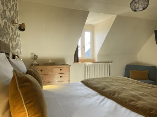 Bright attic bedroom at Hotel Le Trouville with sloped ceiling, wooden dresser, and city views from skylight window