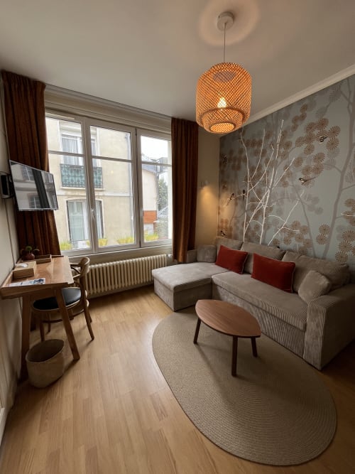 Modern suite at Hotel Le Trouville with beige sofa, wooden desk, pendant light, and city views from large windows